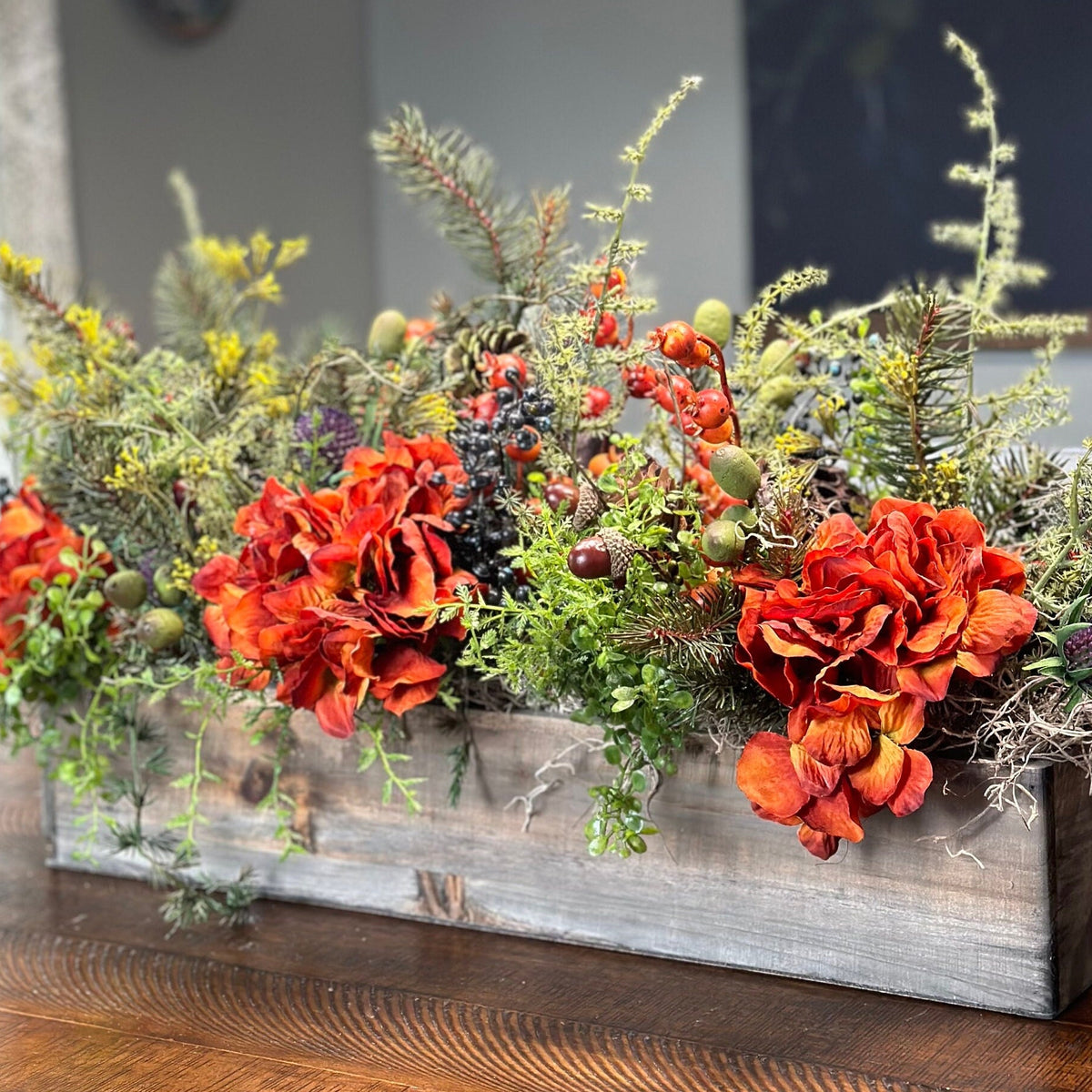 This fall centerpiece is perfect for decorating your table top! It is a grey wash wooden rectangle box 20&quot; long x 9&quot; high by 5&quot; This rustic style arrangement is stunning with orange hydrangeas nestled in greenery with acorns, pinecones and berries