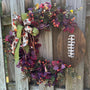 Fall football wreath covered in green and burgandy eucalyptus with burgandy birch leaves. Rustic wooden football, orange and burgandy berries with small velvet green pumpkins nestled in the eucalyptus and topped with bow with footballs to compliment