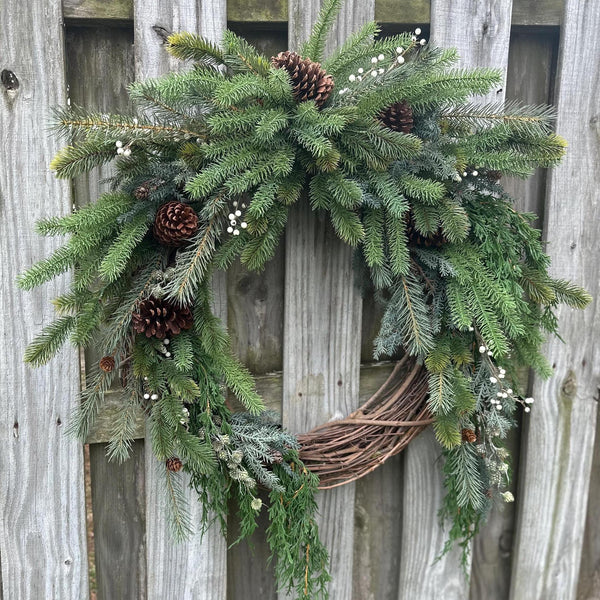 This is a rustic style pine wreath. This wreath is designed on a grapevine base and is covered in diferent pines and also has greenery draping made to look real but is faux to use for years to come. Also has real pinecones and berries nestled in.