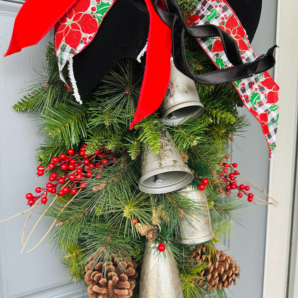 Christmas front door swag with Silver metal bells. Mixed pine with natural pinecones and red berries with twigs topped with a stunning bow!